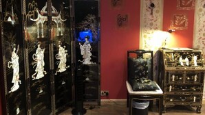 A room with traditional decor, including a mirrored cabinet with artwork, a small table with a lamp, and a decorative chest. - Oriental Suite (Swansea)