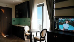A modern hotel room with a dining area, a TV screen displaying a program, and a view through the window. - Atlantis Apartment Nguyen Xuan Khoat (Hanoi)