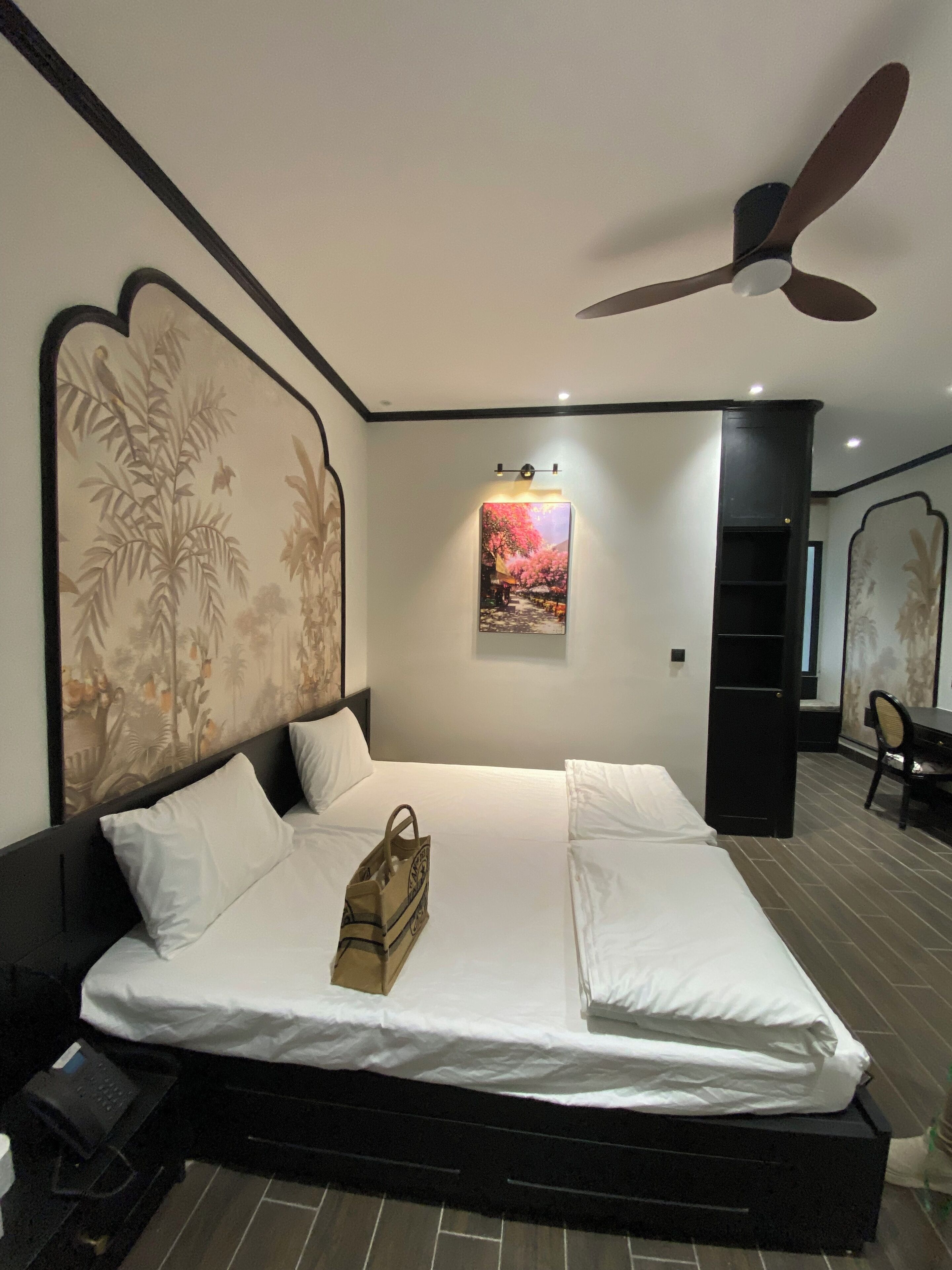 A modern hotel room with a large bed, a ceiling fan, and a painting on the wall.