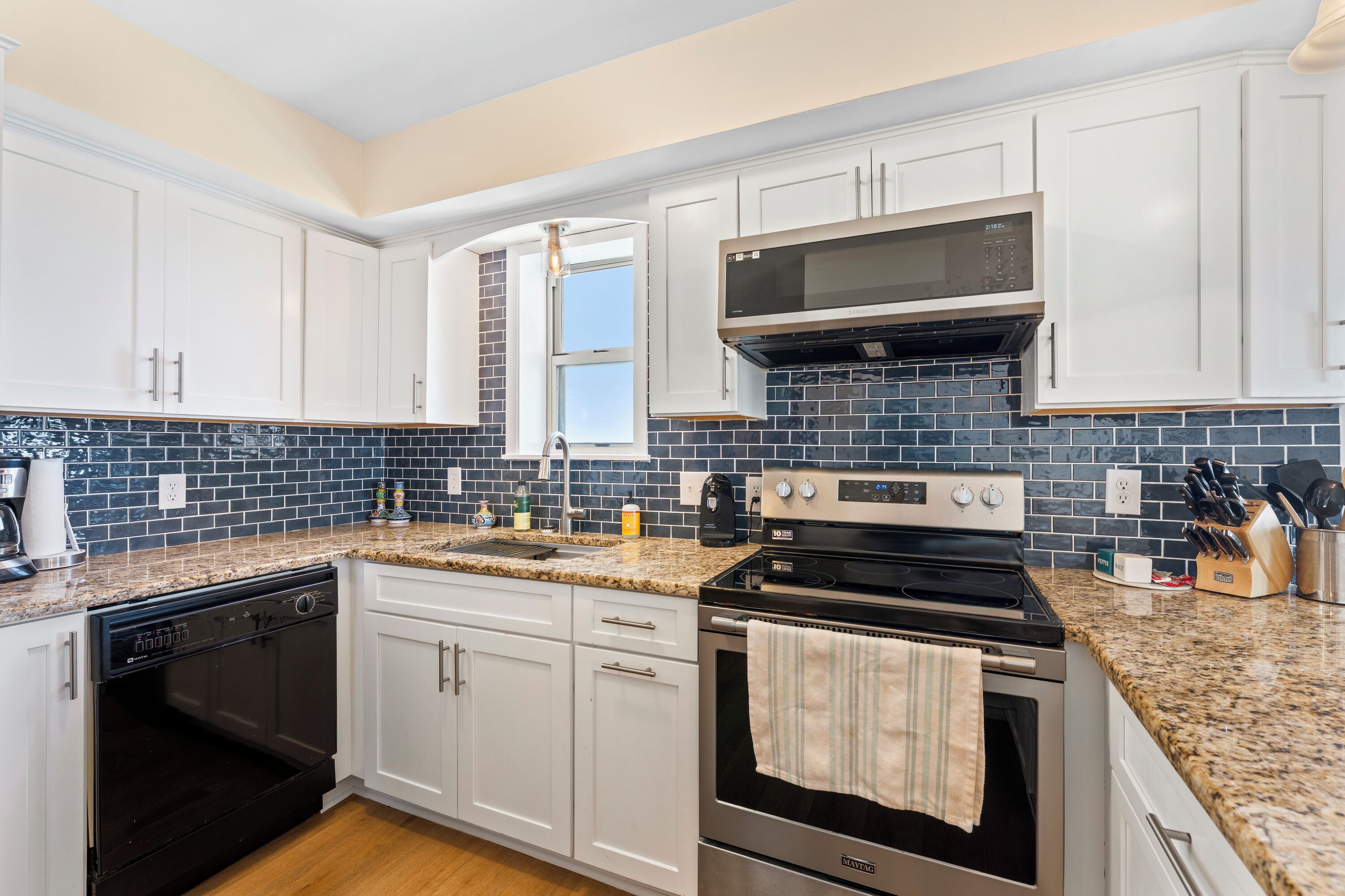 A modern kitchen with white cabinets, a granite countertop, a stainless steel range, and a microwave.