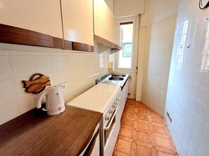 Eine schmale Küche mit weißen Schränken, einer Holzarbeitsplatte und einem Fenster.