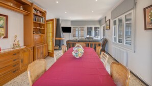 Un coin repas avec une nappe rouge, des meubles en bois, des chaises en osier et une vue sur l’extérieur.