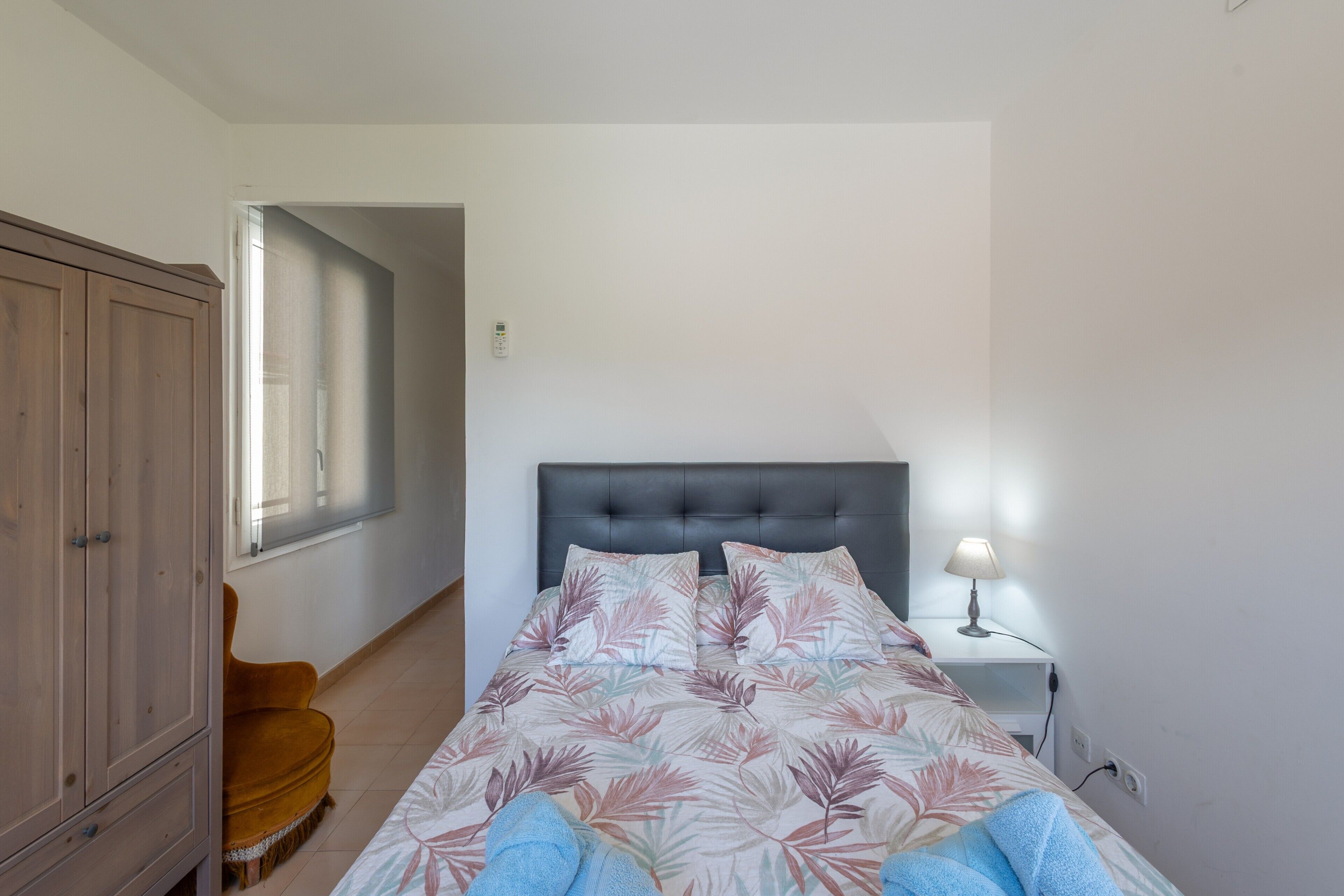 Een slaapkamer met een bed, nachtkastje, lamp, kledingkast en stoel.