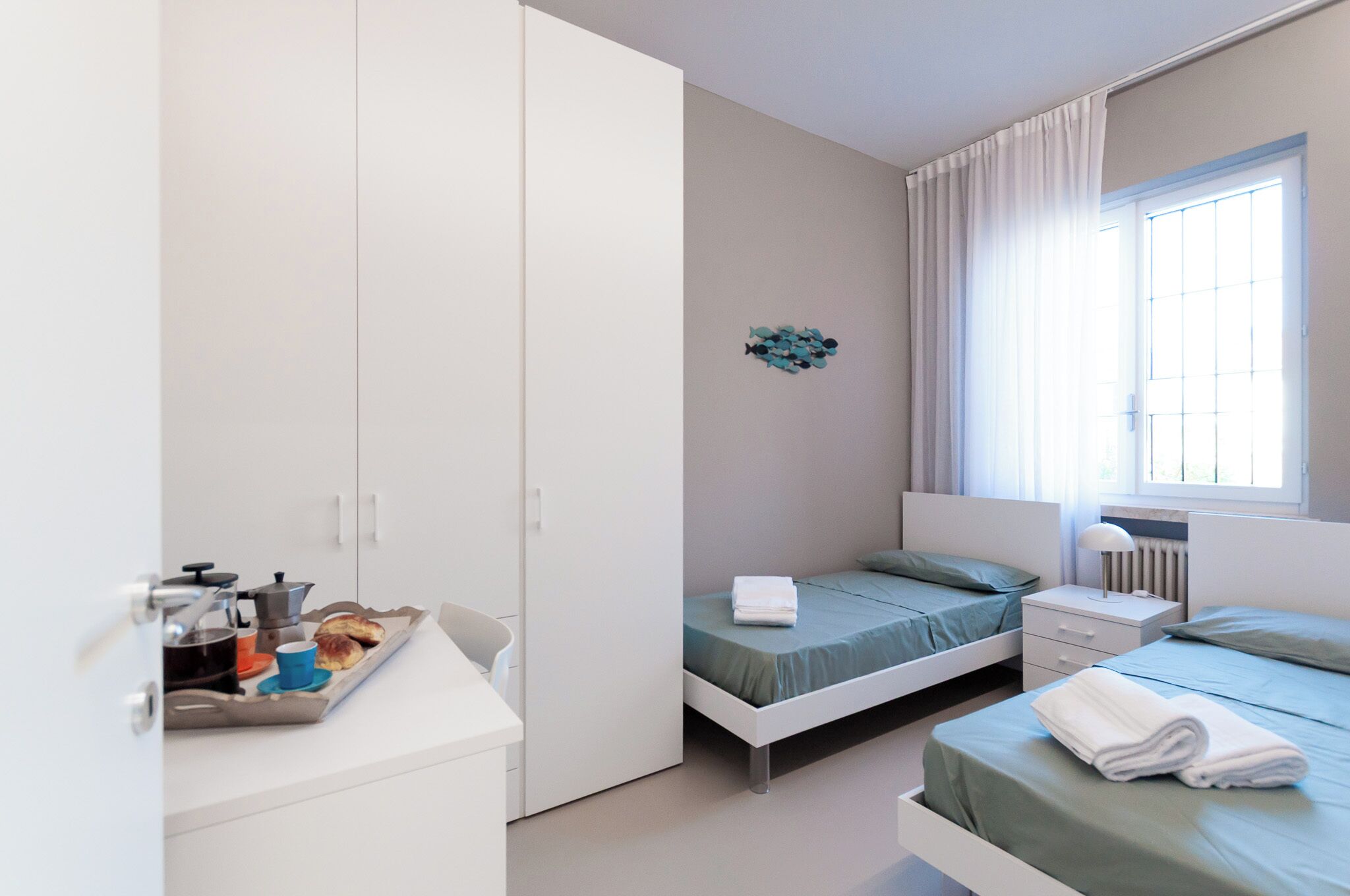 A bedroom with two beds, a wardrobe, a bedside table, and a window with curtains.