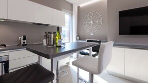 A modern kitchen with white cabinets, a stainless steel countertop, a built-in oven, and a large wall clock. - Aurora Lights Suite (Desenzano del Garda)
