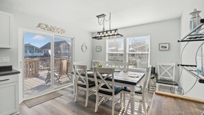 A modern kitchen with white cabinetry, a dining area with a table and chairs, and a view of a balcony with outdoor furniture. - 4BR Channel House-Dock-Linda's Castaway Cottage (North Myrtle Beach)