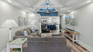A spacious living area with a high ceiling, a kitchen in the background, and a large window overlooking the cityscape. - 4BR Channel House-Dock-Linda's Castaway Cottage (North Myrtle Beach)