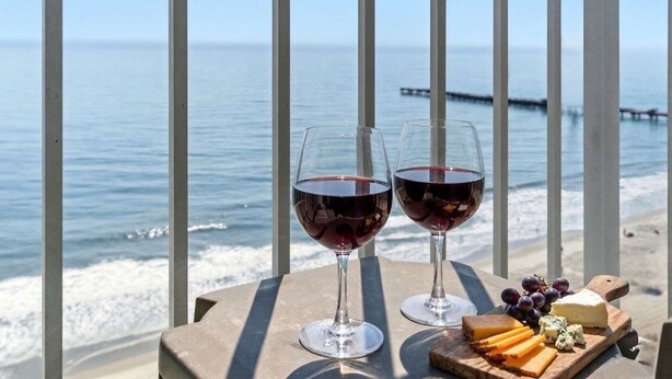 Two wine glasses on a table with a view of the sea and a pier in the background. - Breaker's Boutique Resort 1857- 2BR/2BA- Pool (Myrtle Beach)