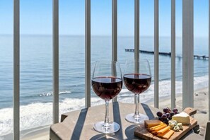 Dos copas de vino sobre una mesa, con vista al mar y un muelle al fondo.