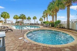 Un área de piscina con dos piscinas, sillas de descanso y palmeras.
