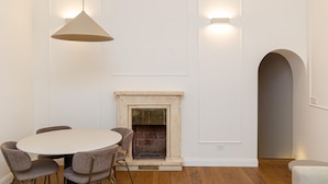 A dining area with a round table, four chairs, a hanging light fixture, a fireplace, and a wall-mounted light. - Trevi Terrace Apartment (Rome)
