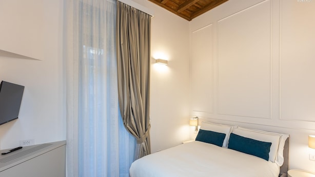 A bedroom with a bed, bedside lamps, a TV, and a window with curtains. - Trevi Terrace Apartment (Rome)