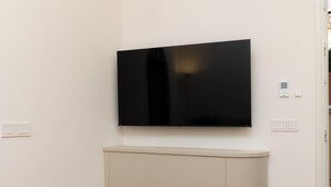 A modern room with a flat-screen TV mounted on the wall, a light-colored cabinet below, and a thermostat on the wall. - Trevi Terrace Apartment (Rome)