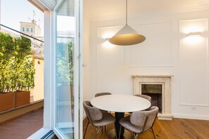 A dining area with a round table and four chairs, a hanging light fixture, and a fireplace. - Trevi Terrace Apartment (Rome)