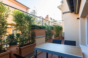 Ein Balkon mit Tisch und Stühlen, umgeben von Topfpflanzen und Blick auf benachbarte Gebäude.