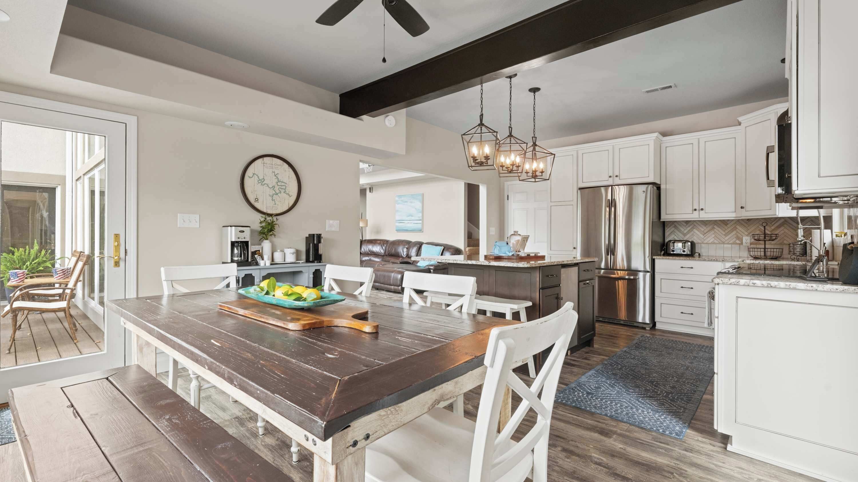 A modern kitchen with white cabinets, a stainless steel refrigerator, and a dining area with a wooden table and white chairs.