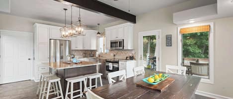 Una cocina moderna con armarios blancos, una isla central con taburetes y una mesa de comedor con frutero.