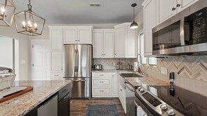 A modern kitchen with white cabinetry, stainless steel appliances, and a herringbone tile backsplash. - Mimosa Mornings Home for 12 (Eldon)