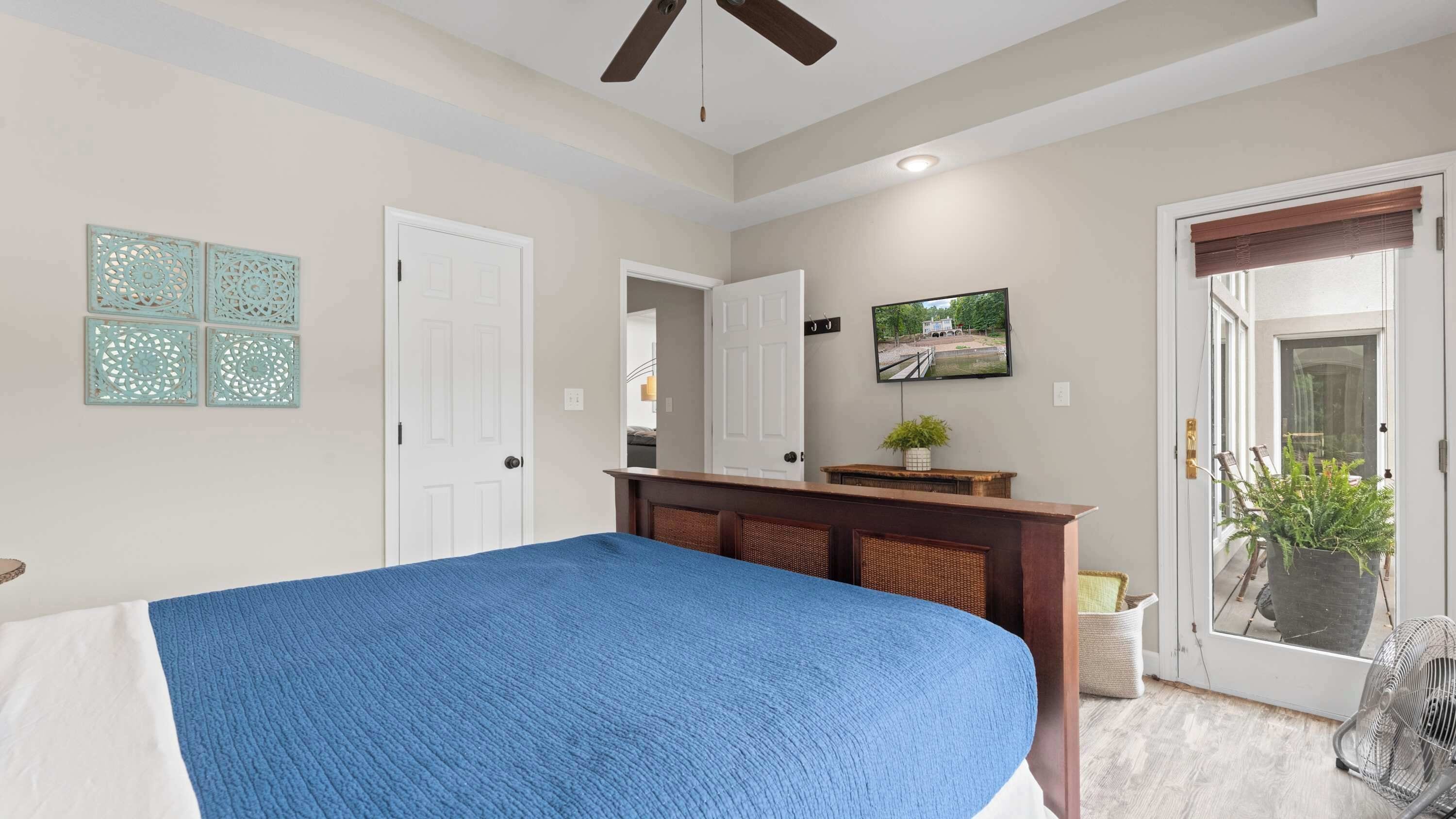 Een slaapkamer met een bed, een dressoir, een televisie en een deur naar een balkon.