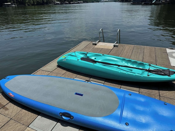 Un kayak et une planche à pagaie sur un quai, au bord d’une étendue d’eau calme.