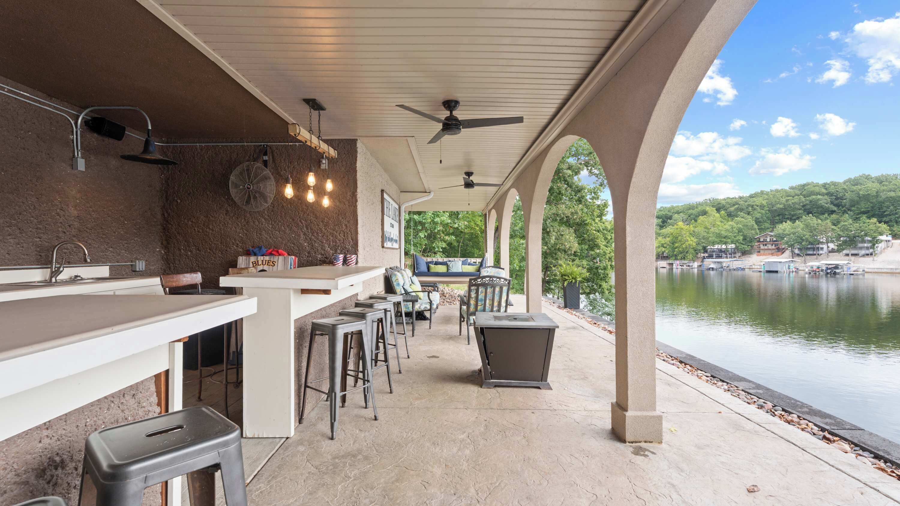 An outdoor bar area with a view of a lake, seating, and a fan.