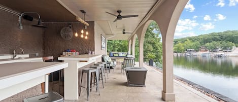An outdoor bar area with a view of a lake, seating, and a fan.