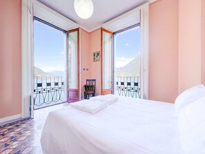 Ein Schlafzimmer mit einem großen Bett, einem Sessel und Blick auf einen Balkon mit Geländer.