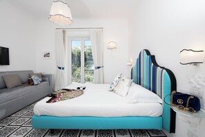 Un dormitorio con cama, sofá, ventana con cortinas y una lámpara de pared.