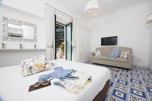 Ein Schlafzimmer mit einem großen Bett, einer Couch, einem Fernseher und einem Balkon mit Vorhängen.