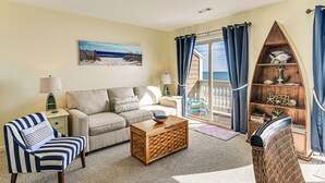 Ein Wohnzimmer mit einer Couch, einem gestreiften Sessel, einem Holztisch, einem Bücherregal und einem Bild von einer Strandlandschaft.