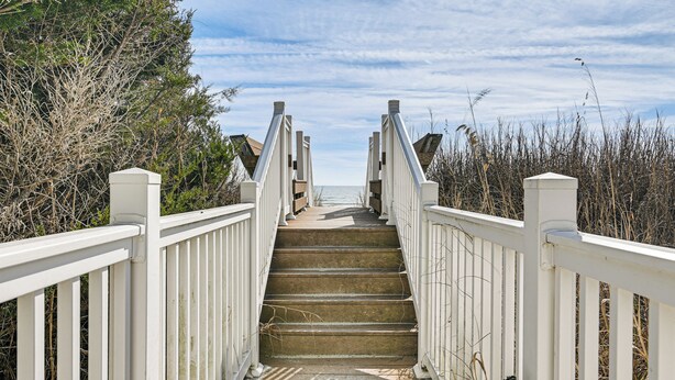 Eine Holztreppe mit weißen Geländern führt zu einem Strand.