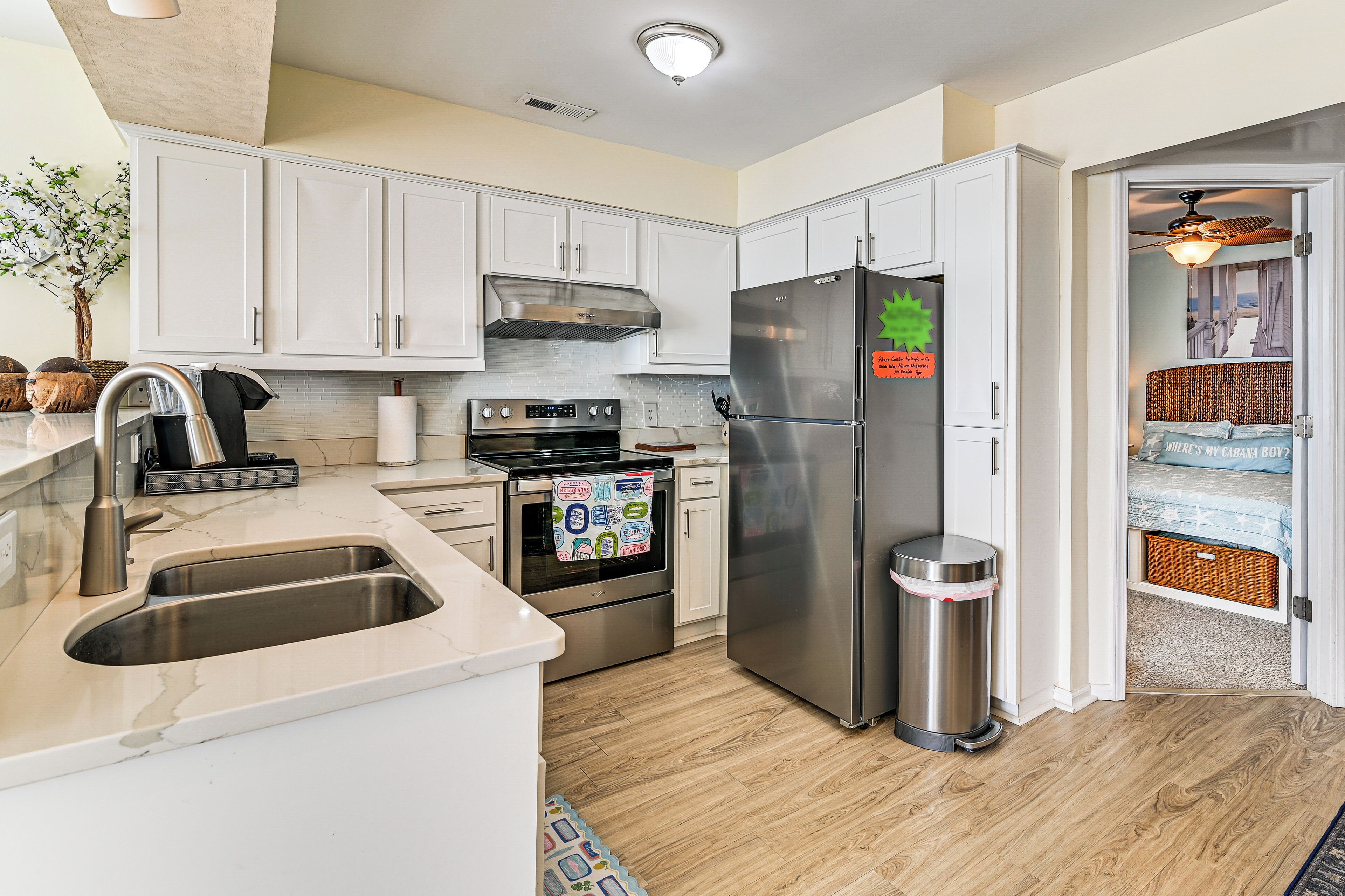 A modern kitchen with white cabinets, stainless steel appliances, and a wooden floor.
