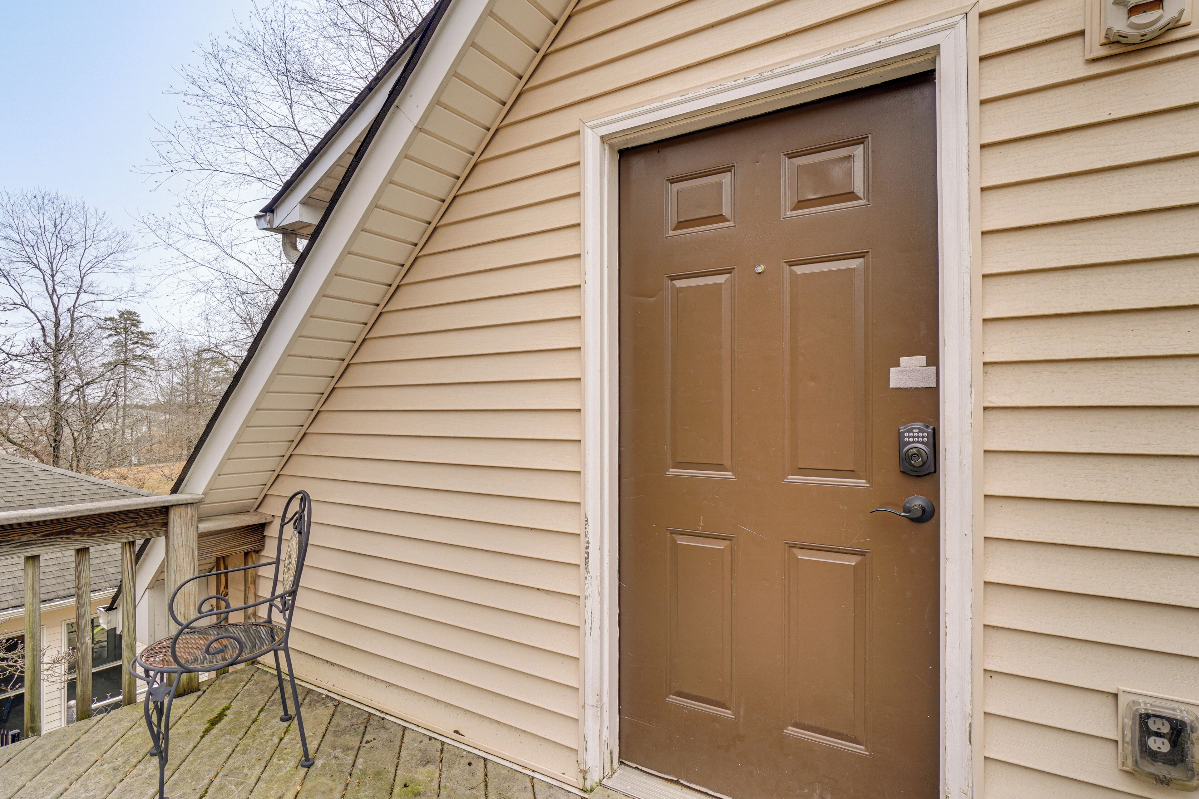 A brown front door with a keypad lock, beige siding, and a small porch with a metal chair.