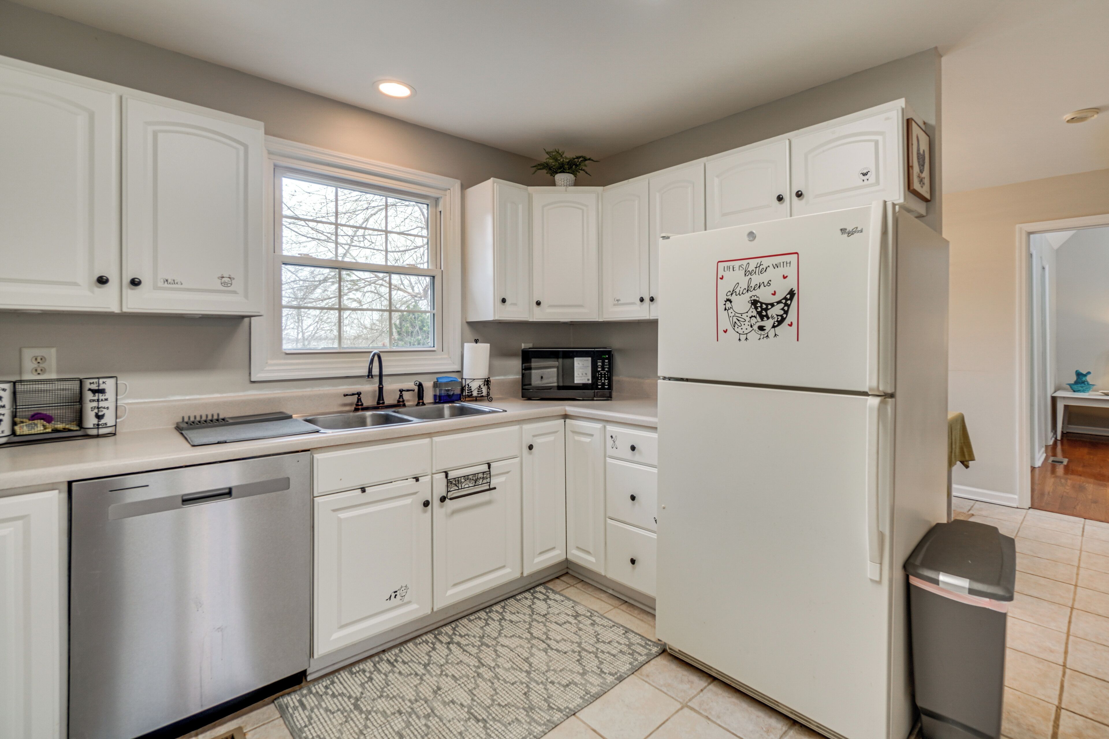A kitchen with white cabinets, a stainless steel dishwasher, a microwave, and a refrigerator with a dog sticker.