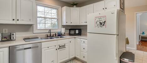 A kitchen with white cabinets, a stainless steel dishwasher, a microwave, and a refrigerator with a dog sticker.