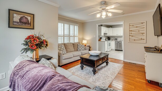 A living room with a sofa, coffee table, and a vase of flowers. There is a ceiling fan and a kitchen visible in the background. - Knoxville Farmhouse Retreat! Easy Access to Town (Knoxville)