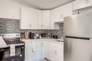 A modern kitchen with white cabinets, a stainless steel refrigerator, a microwave, and a stove. - 2 Mi to Busch Gardens! Family Getaway in Tampa (Tampa)
