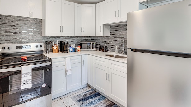 A modern kitchen with white cabinets, a stainless steel refrigerator, a microwave, and a stove. - 2 Mi to Busch Gardens! Family Getaway in Tampa (Tampa)