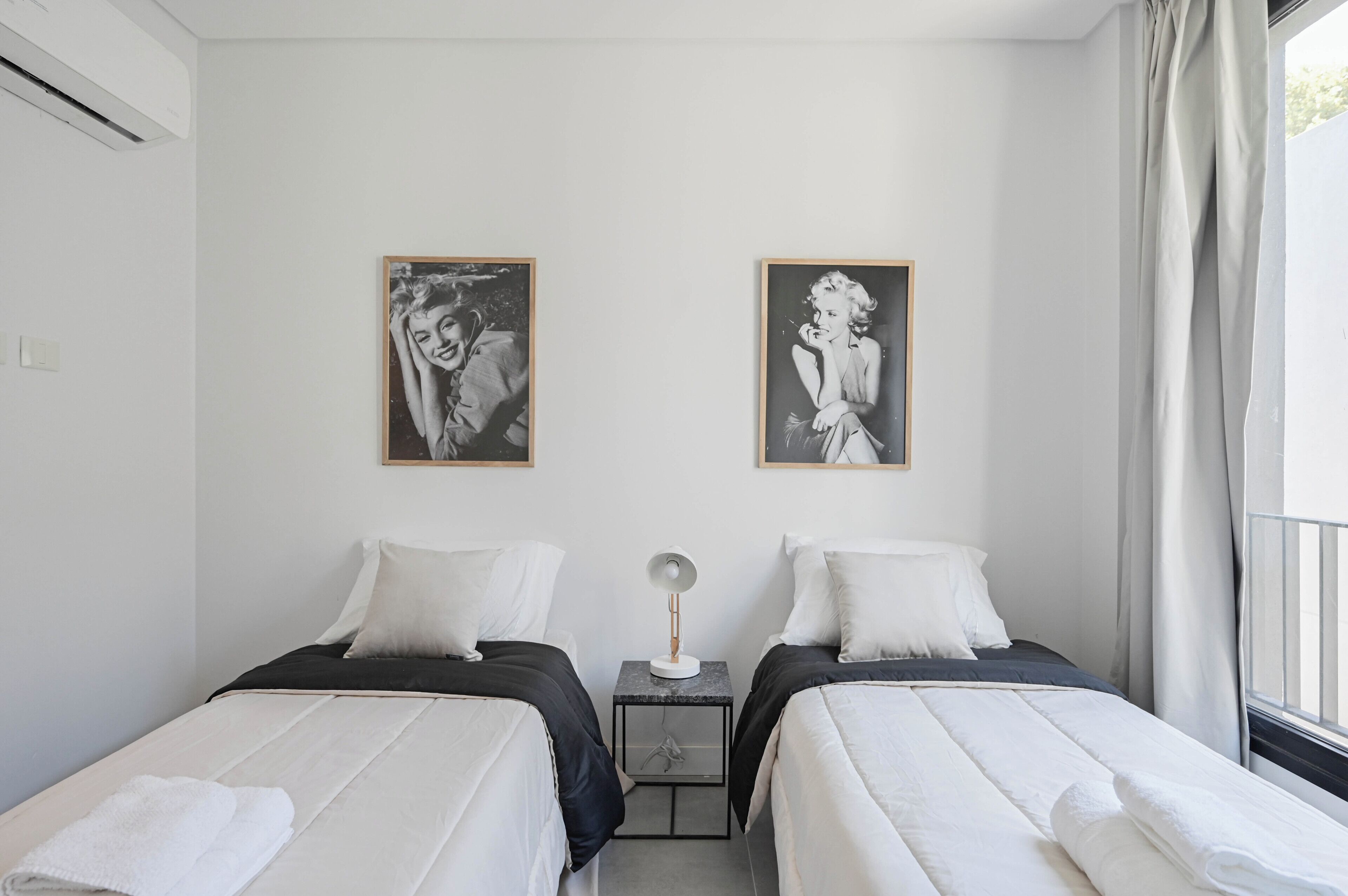 A hotel room with two beds, a nightstand with a lamp, and two framed pictures on the wall.