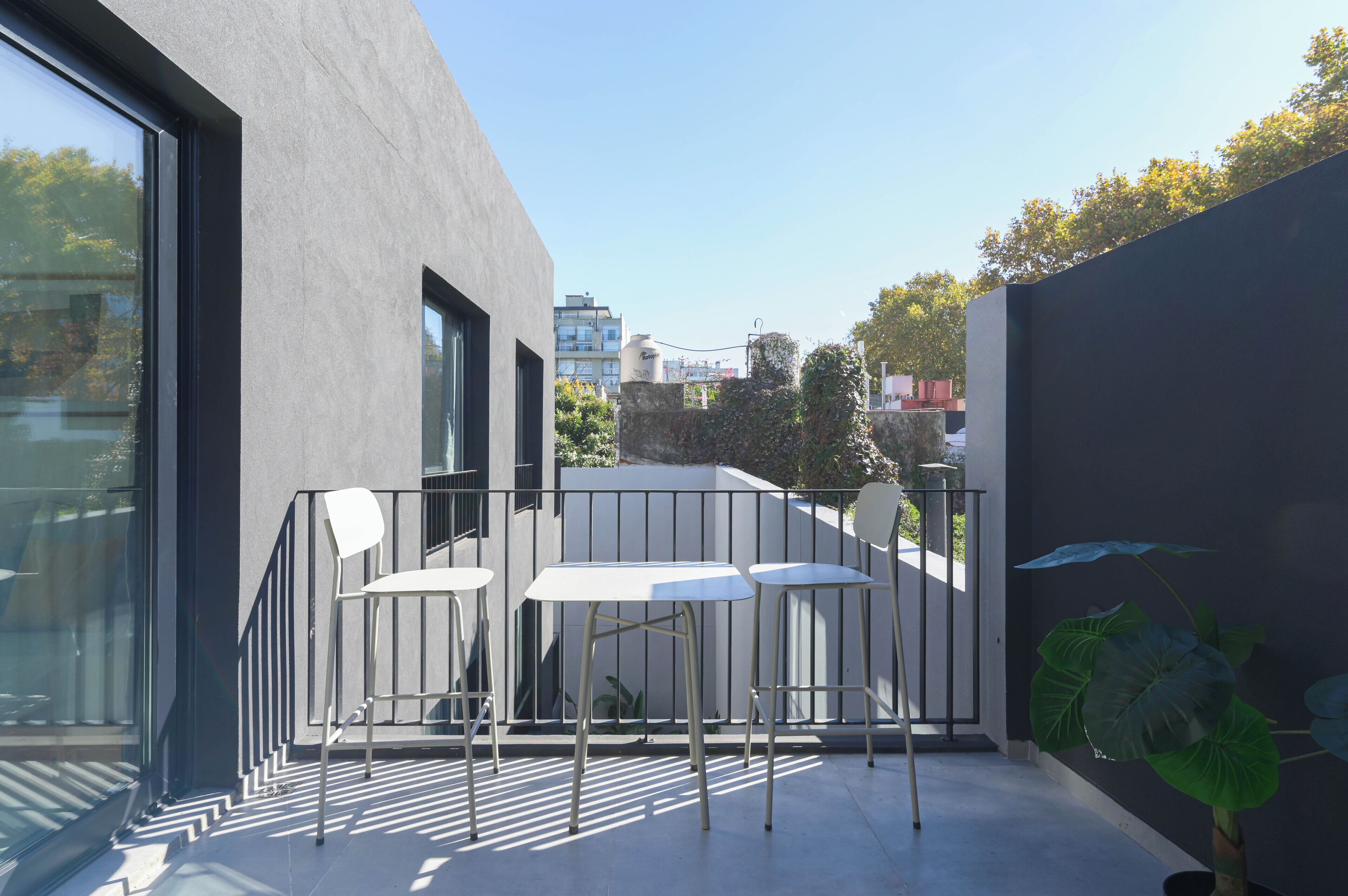 Un patio exterior moderno con diseño minimalista, que incluye una mesa, sillas, una planta en maceta y vistas de la ciudad.