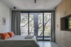 A bedroom with a bed, curtains, a TV, and a view of trees through large windows. - MOT Black Ravignani (Buenos Aires)