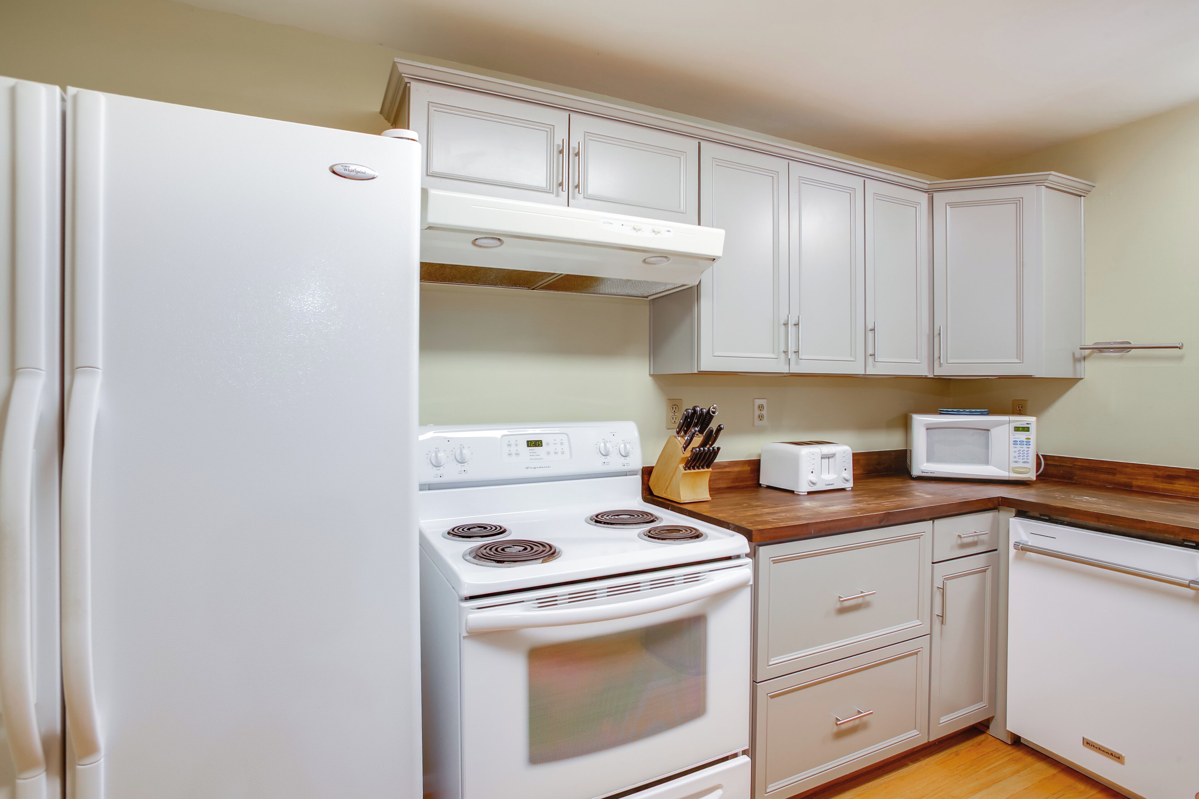 Una cocina con electrodomésticos blancos, encimeras de madera y armarios de tonos claros.