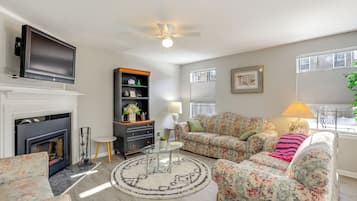 A living room with a fireplace, floral sofa, round coffee table, and a flat-screen TV mounted above the fireplace.