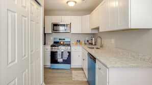 Una cocina con armarios blancos, una estufa azul y un lavamanos de acero inoxidable.