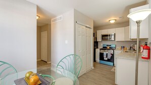 Una cocina moderna con armarios blancos, una estufa azul y un microondas. Hay una zona de comedor con una mesa de vidrio y sillas verdes.
