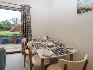 A dining area with a table set for four, chairs, a window with curtains, and a view of the garden. - Cairndhu (Bo'ness)