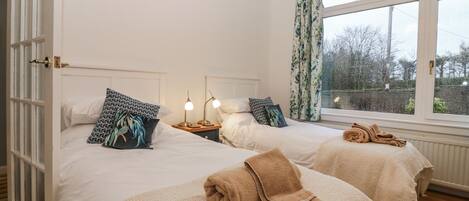 A bedroom with two beds, a window with curtains, and a view of trees outside.