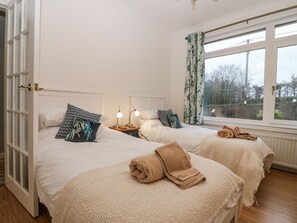 A bedroom with two beds, a window with curtains, and a view of trees outside. - Cairndhu (Bo'ness)