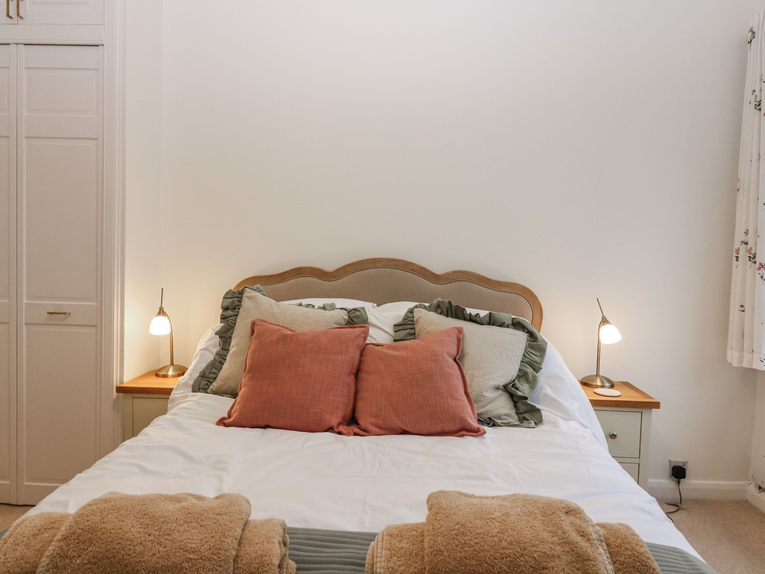 Cama bem arrumada com duas almofadas, duas luminárias de cabeceira e cabeceira de madeira.