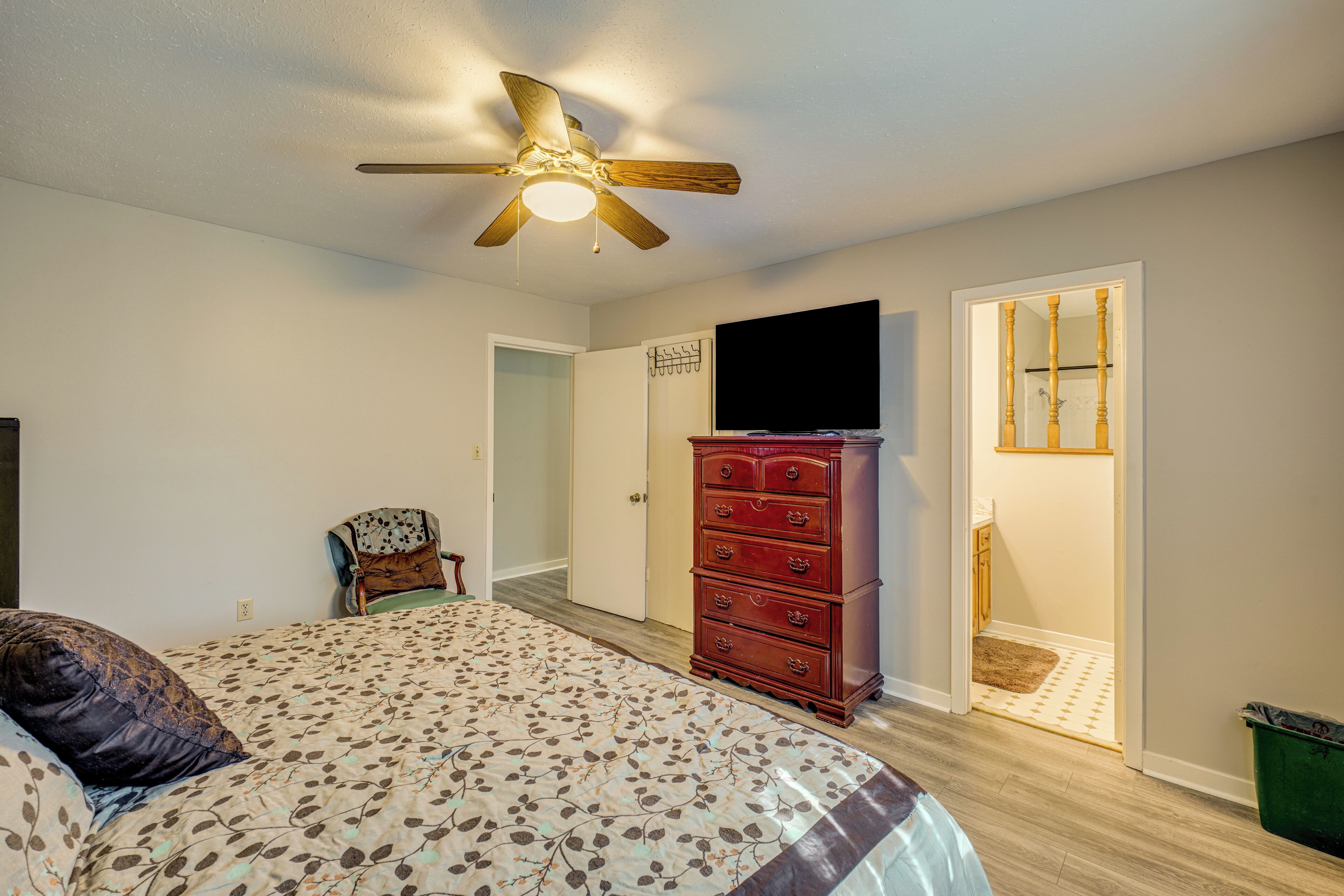 A bedroom with a bed, a dresser, a ceiling fan, and a television.
